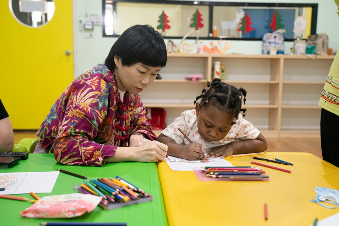 An adult and a child drawing together at a colorful classroom table.